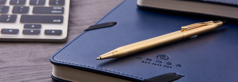 Classic Century 23KT Gold-Plated Ballpoint Pen resting on a Cross Midnight Blue journal.