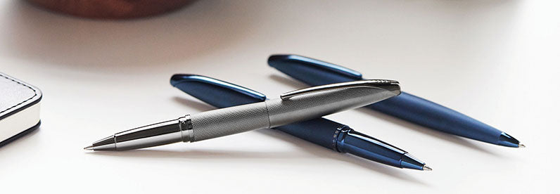 Three ATX pens stacked on top of each other, including the Sandblasted Dark Blue PVD Rollerball and Ballpoint Pens, with the Sandblasted Titanium Grey PVD Rollerball pen on top.