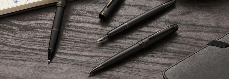 Bailey Matte Black Ballpoint, Rollerball, and Fountain Pens spread out on a desk.