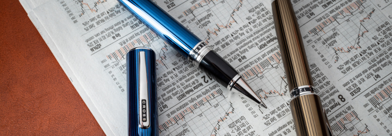 Peerless Translucent Quartz Blue Rollerball Pen uncapped and Peerless Translucent Grey Pen resting on a newspaper.
