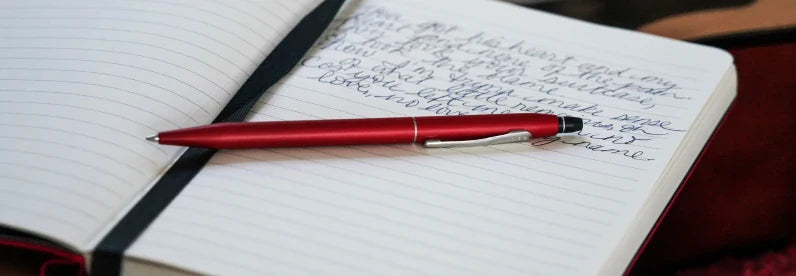 Click Crimson Ballpoint Pen resting on an open Cross journal.